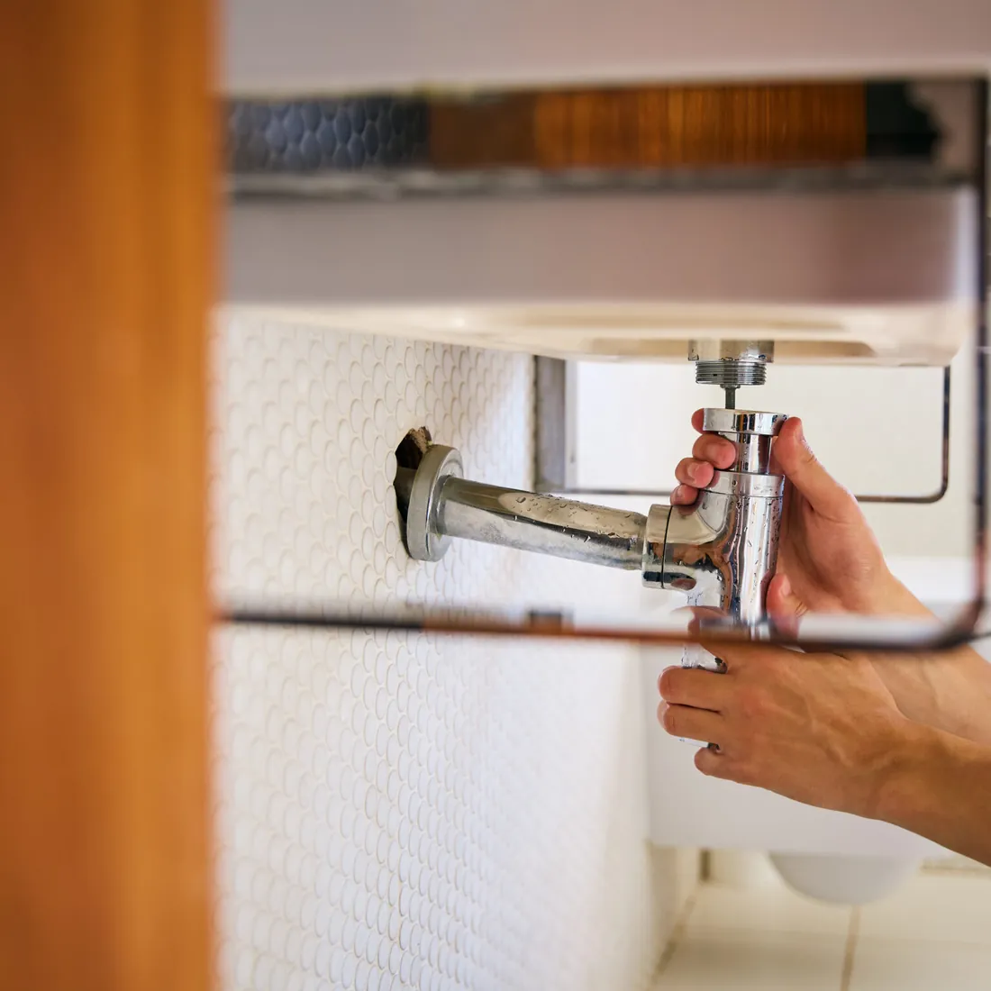 Plumber tightening a leaking pipe fitting under a sink